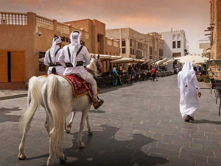 Image of two men dressed in the Qatari national dress strolling on horseback at Souq Waqif, Doha.